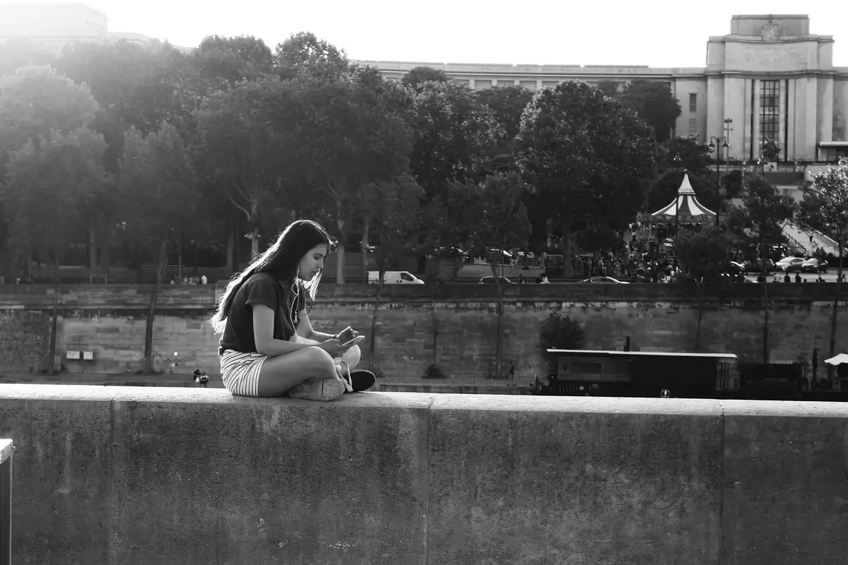 Ragazza adolescente seduta su un muretto mentre guarda lo smartphone, in bianco e nero
