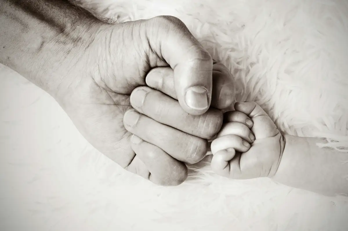 Mano di un adulto che stringe la manina di un neonato, in bianco e nero