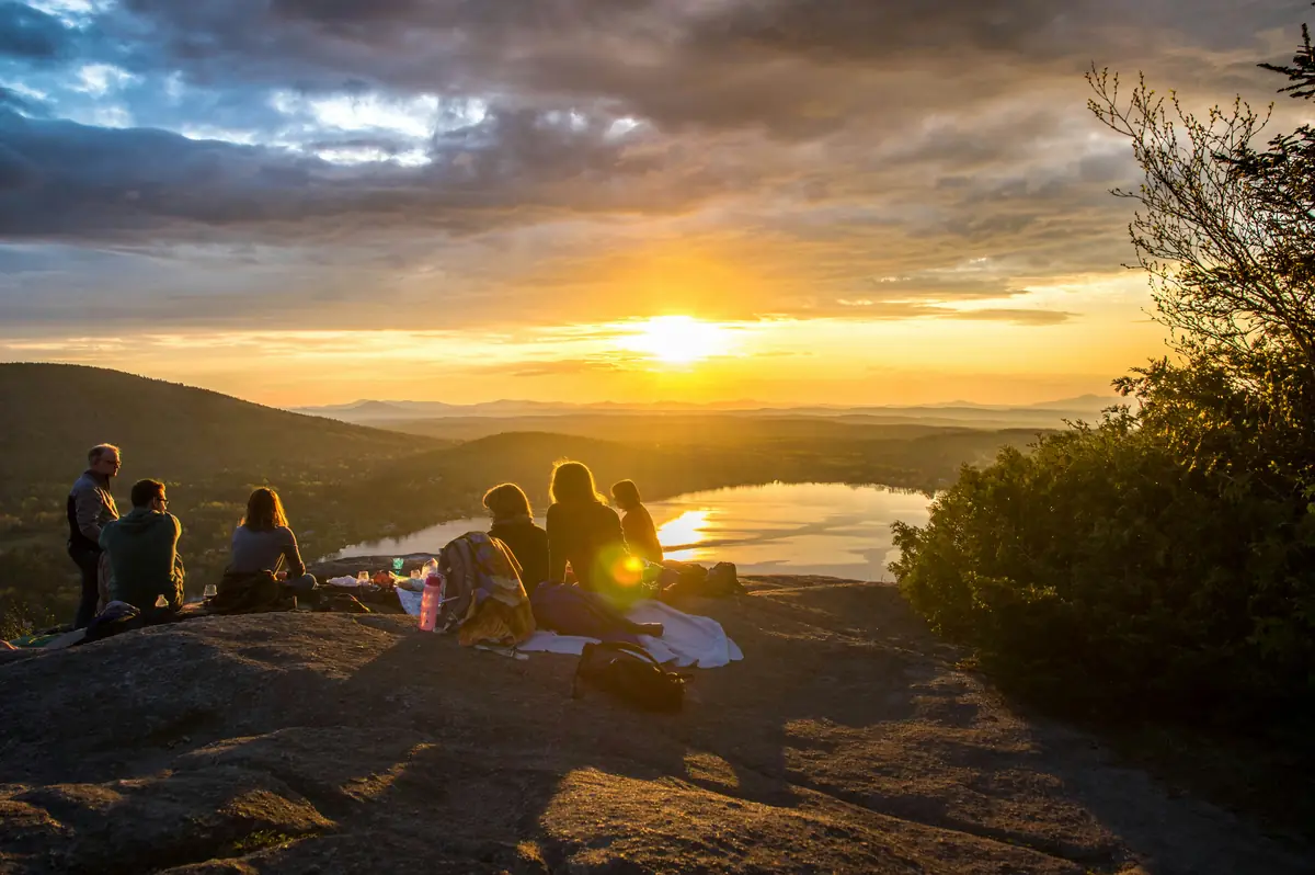 Gruppo di persone sedute su una cima al tramonto guardando un lago